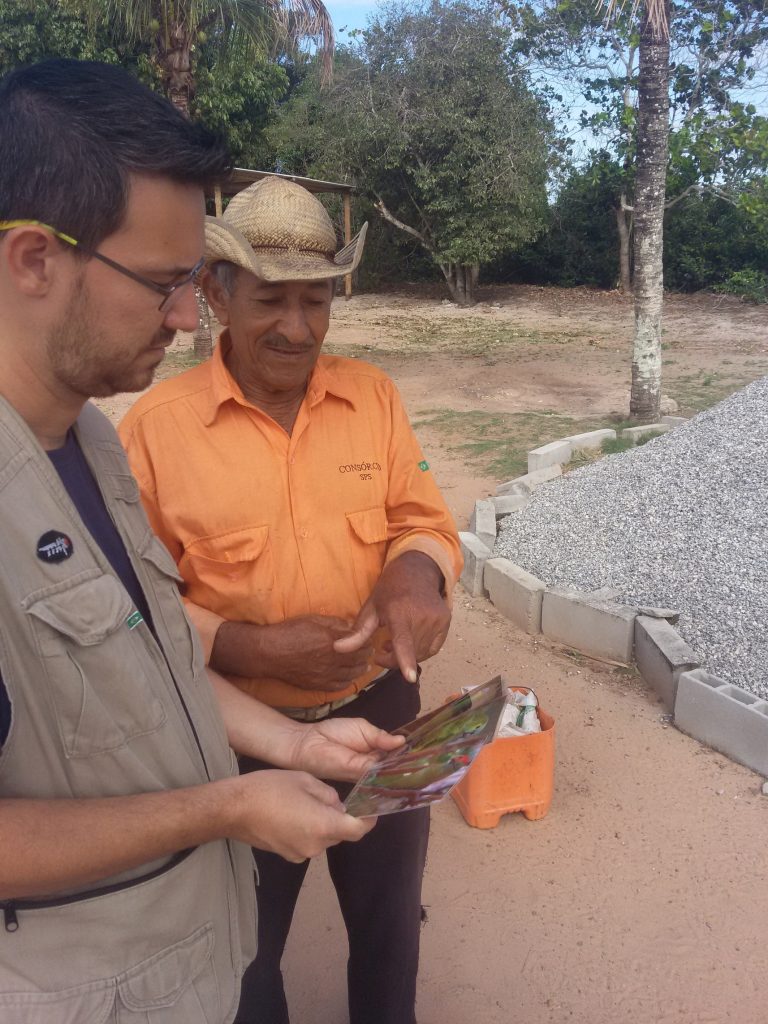 Pesquisador do Projeto Chauá mostrando material educativo sobre aves para um morador em uma área rural.