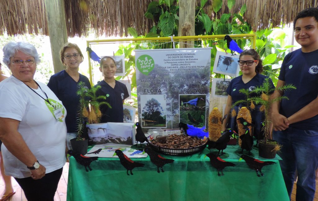 Grupo de pessoas em uma exposição sobre a conservação da Mata Atlântica, cercada por plantas e uma mesa com materiais expositivos do Projeto SOS Fauna.