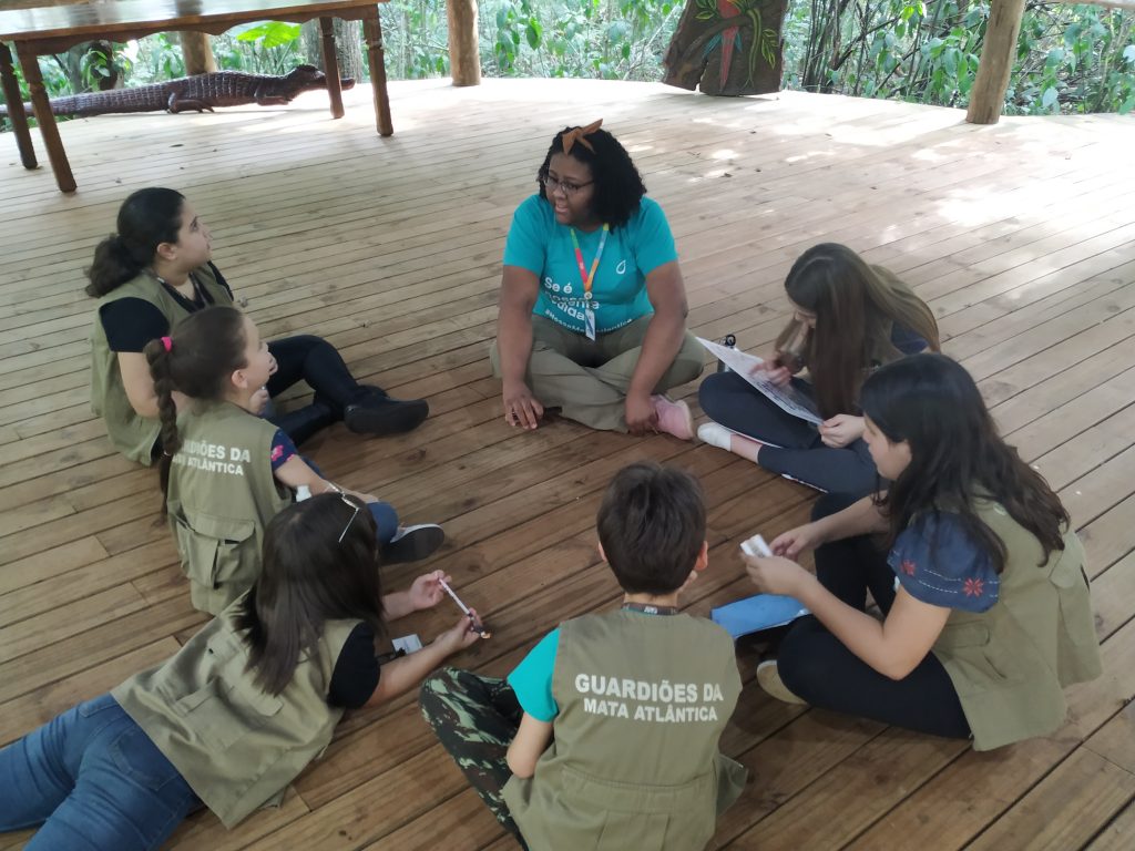 Educadora ambiental sentada em cículo com crianças