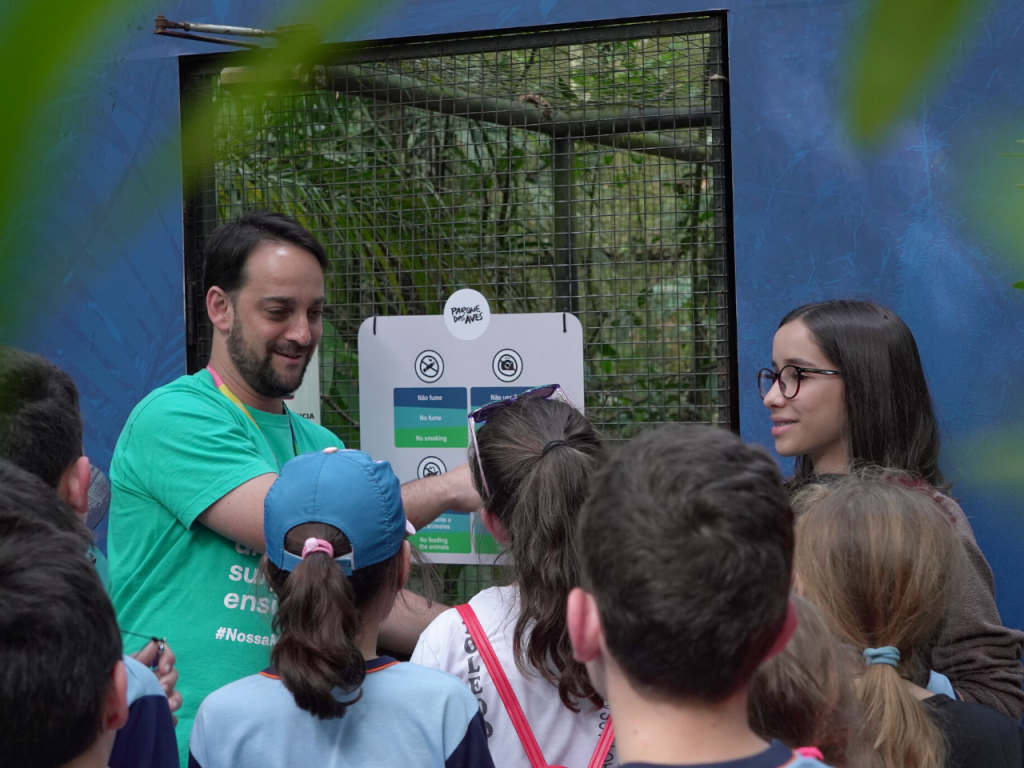 Mediador de trilha orientando visitantes na entrada de um viveiro no Parque das Aves