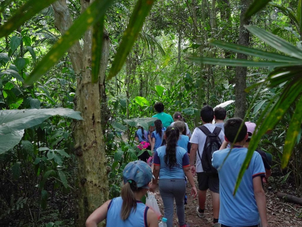 Educador Ambiental do Parque das Aves com os alunos em meio a uma trilha na mata 