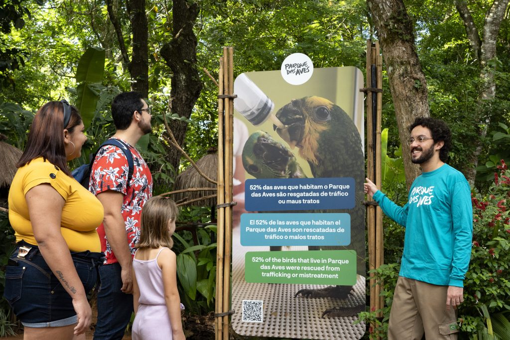 Educador ambiental do Parque das Aves em frente a uma placa. 52% das aves são resgatas do tráfico ou maus tratos.