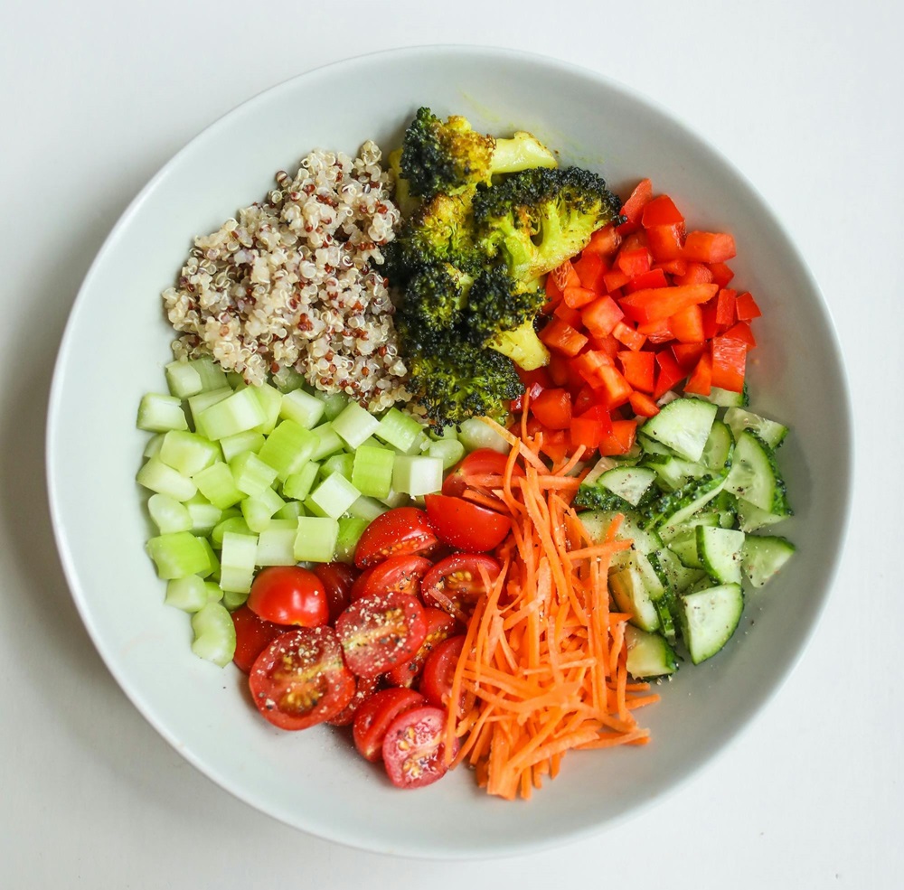 Prato com alimentos saudáveis como quinoa, brócolis, pimentão, pepino, cenoura, tomate e aipo.