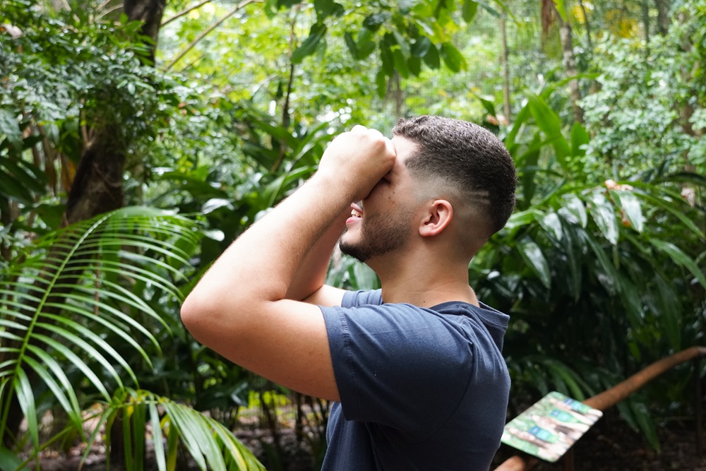 Visitante observando o alto com as mãos em concha nos olhos, em meio à vegetação exuberante do Parque das Aves em meio a Mata Atlântica.