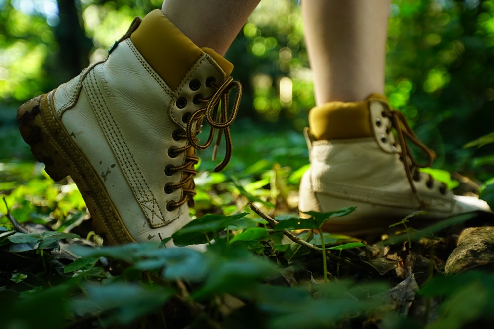 Pessoa caminhando em trilha na floresta com botas de caminhada claras, cercada por vegetação verde da Mata Atlântica.