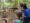 Educadora do Parque das Aves com pintura facial azul aponta algo na trilha enquanto conversa com uma criança segurando uma prancheta de observação.