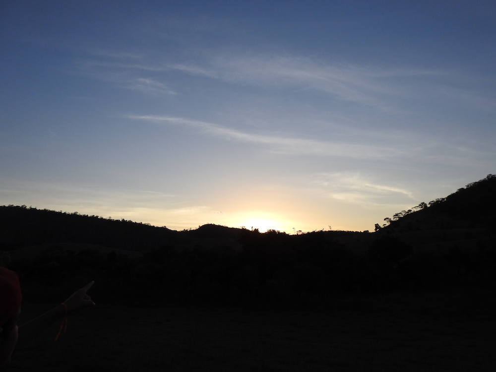 Imagem de um pôr do sol, com o céu em tons de azul e laranja sobre uma paisagem de colinas escuras ao fundo.