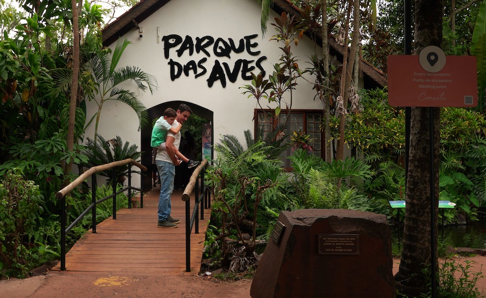 Filho montado nas costas do seu pai em frente da entrada do Parque das Aves.