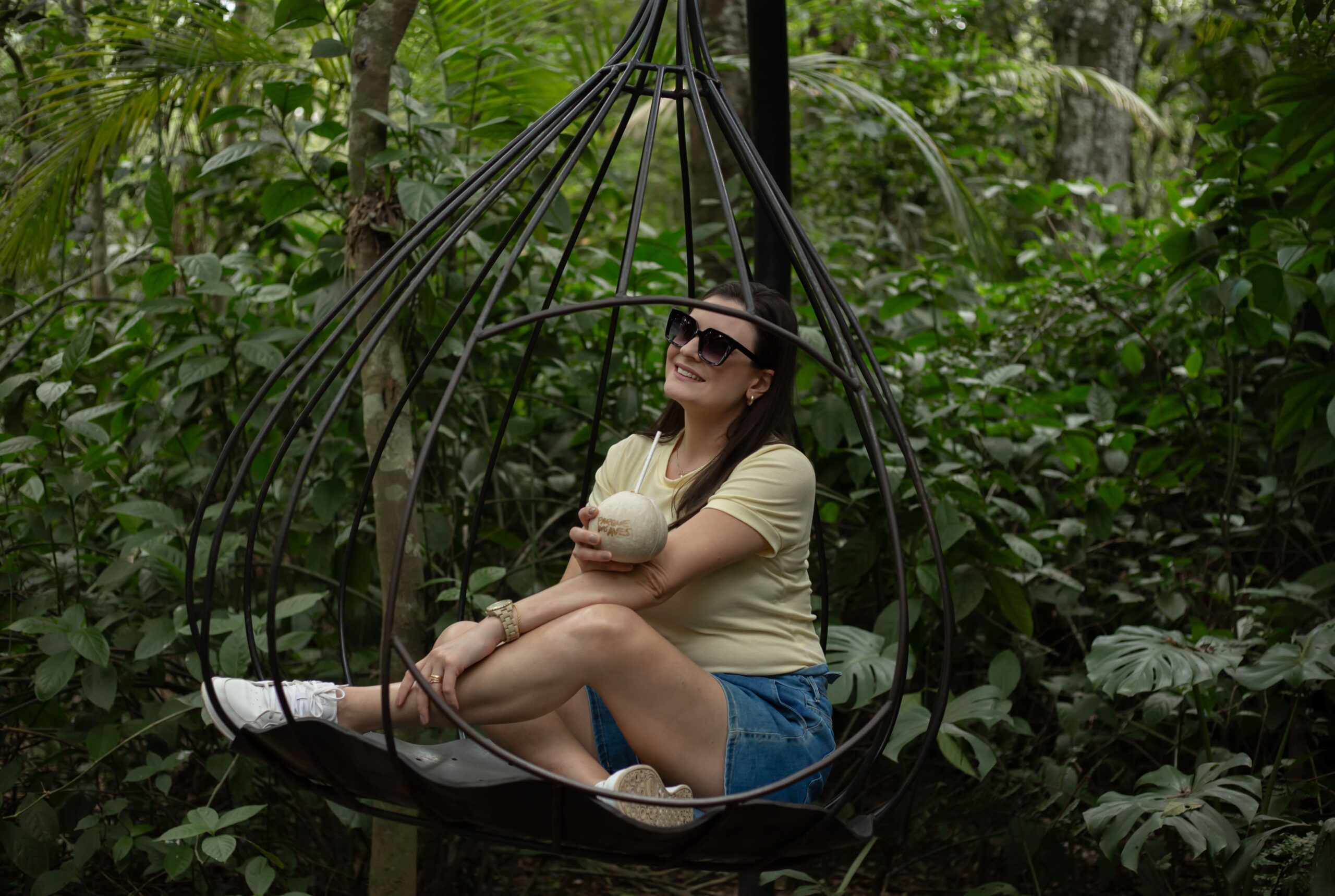 Modelo mulher jovem adulta visitante sentada sorrindo tcom água de coco no balanço ponto instagramável