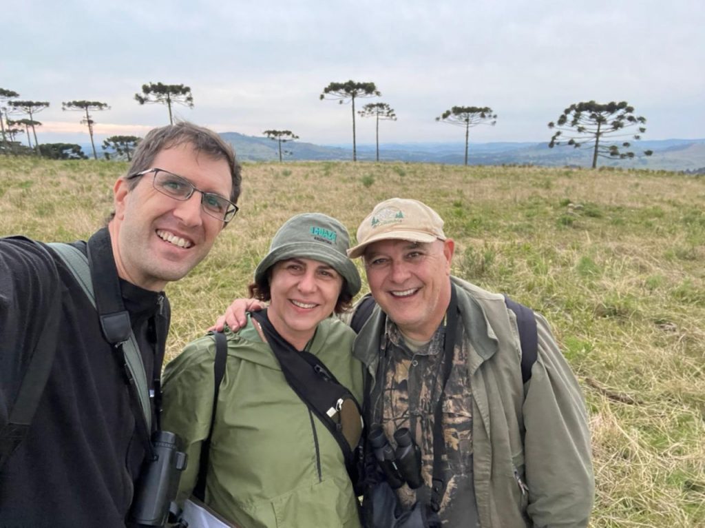Ben Phalan, chefe de conservação do Parque das Aves, ao lado de Nêmora Prestes e Jaime Martinez, coordenadores do Projeto Charão. Atrás deles podemos ver árvores araucárias.