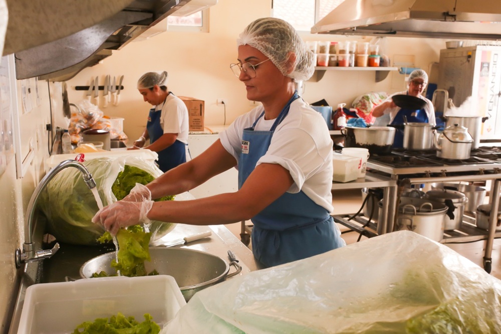Colaboradoras do setor de alimentação do Parque das Aves usando aventais e toucas enquanto preparam refeições na cozinha.