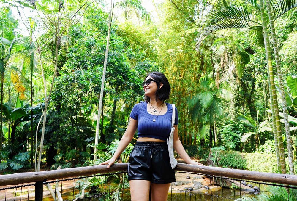 Mulher sorridente em uma ponte do Parque das Aves, rodeada por vegetação exuberante ao fundo.