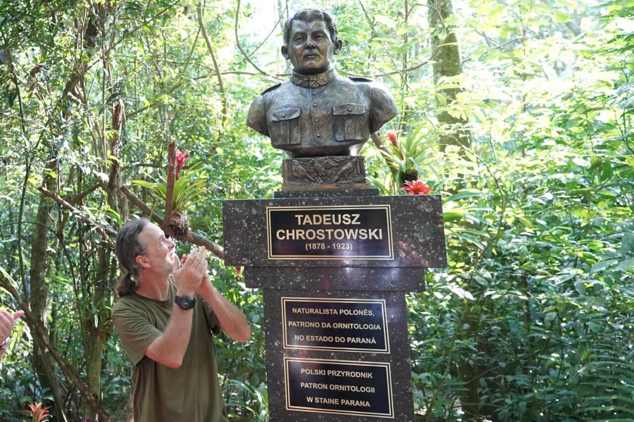 Homem aplaude em frente ao busto de Tadeusz Chrostowski, naturalista polonês e patrono da ornitologia no Paraná, instalado em meio à vegetação do Parque das Aves