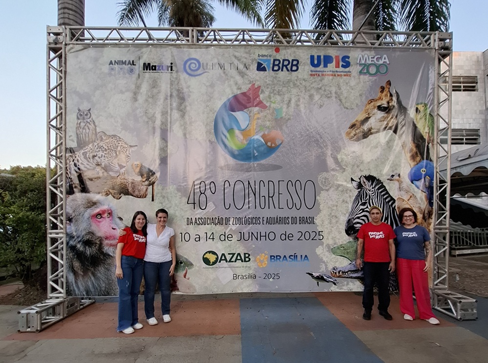 Equipe do Parque das Aves posando em frente ao banner oficial do 48º Congresso da AZAB, em Brasília.