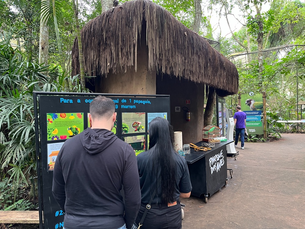 Visitantes observam painéis educativos sobre tráfico de animais em área temática do Parque das Aves.