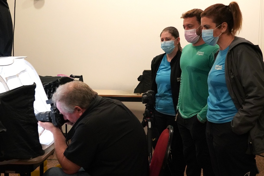 Colaboradores do Parque das Aves observam o fotógrafo Joel Sartore fotografando um animal pequeno em estrutura iluminada do Photo Ark.