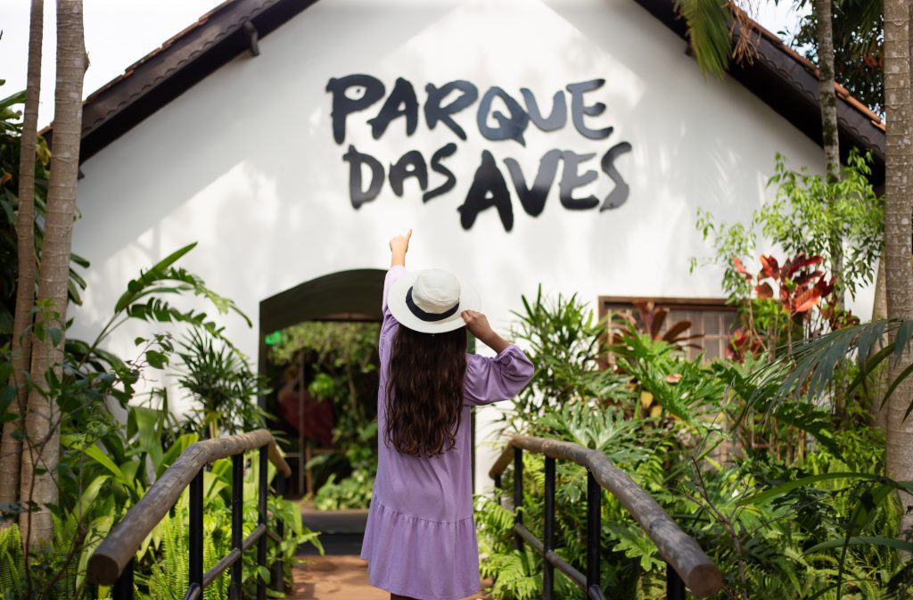 Criança aponta para a entrada do Parque das Aves, em Foz do Iguaçu, durante visita em família.